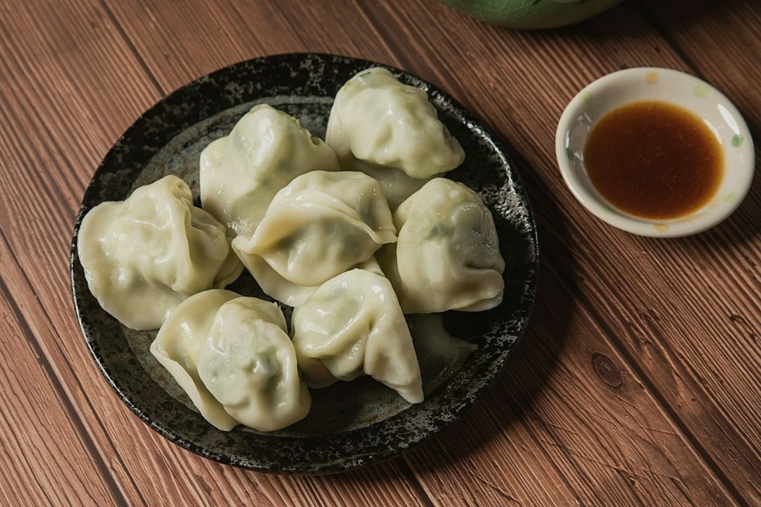 Steamed dumplings served with soy sauce on a ceramic plate.